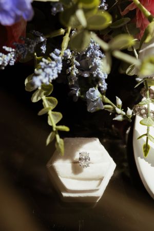 White wedding ring box with delicate floral arrangements and greenery in soft lighting.