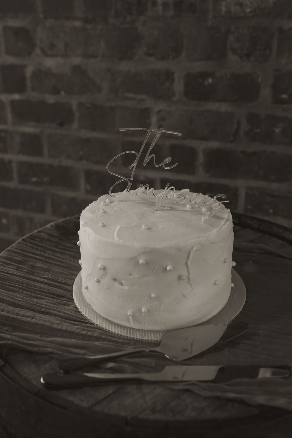 A simple white frosted wedding cake on a dark wooden surface.
