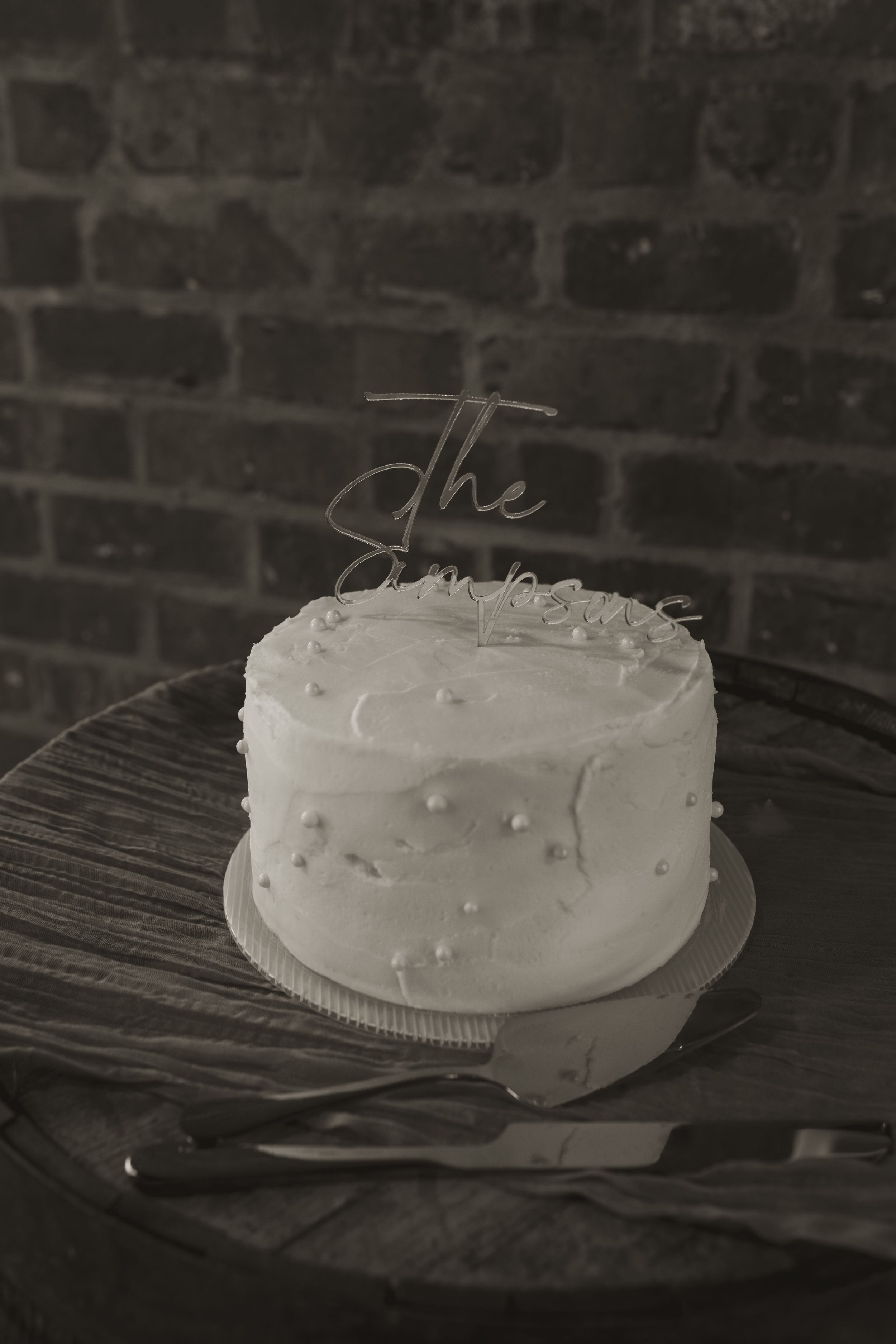 A simple white frosted wedding cake on a dark wooden surface.