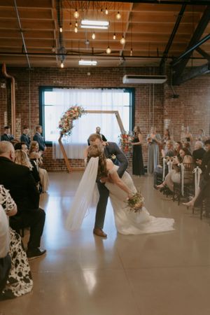 Wedding ceremony in industrial brick venue with exposed beams and large windows.