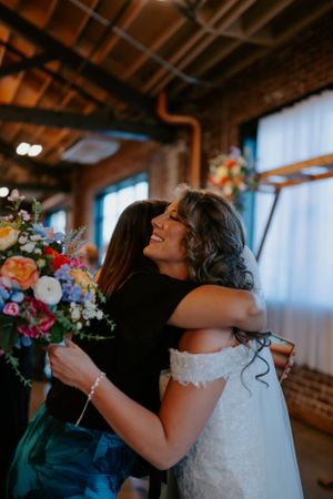 Emotional embrace during wedding reception in rustic brick-walled venue.