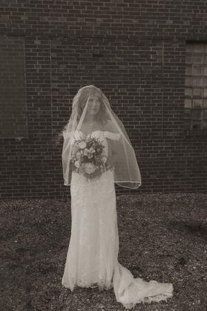 A white wedding dress with veil and floral crown displayed against a brick wall background.