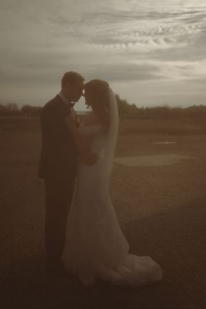 Romantic silhouette of couple embracing at sunset in open field.