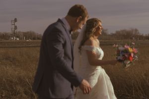 A couple embraces during their outdoor wedding ceremony in a rustic field setting.