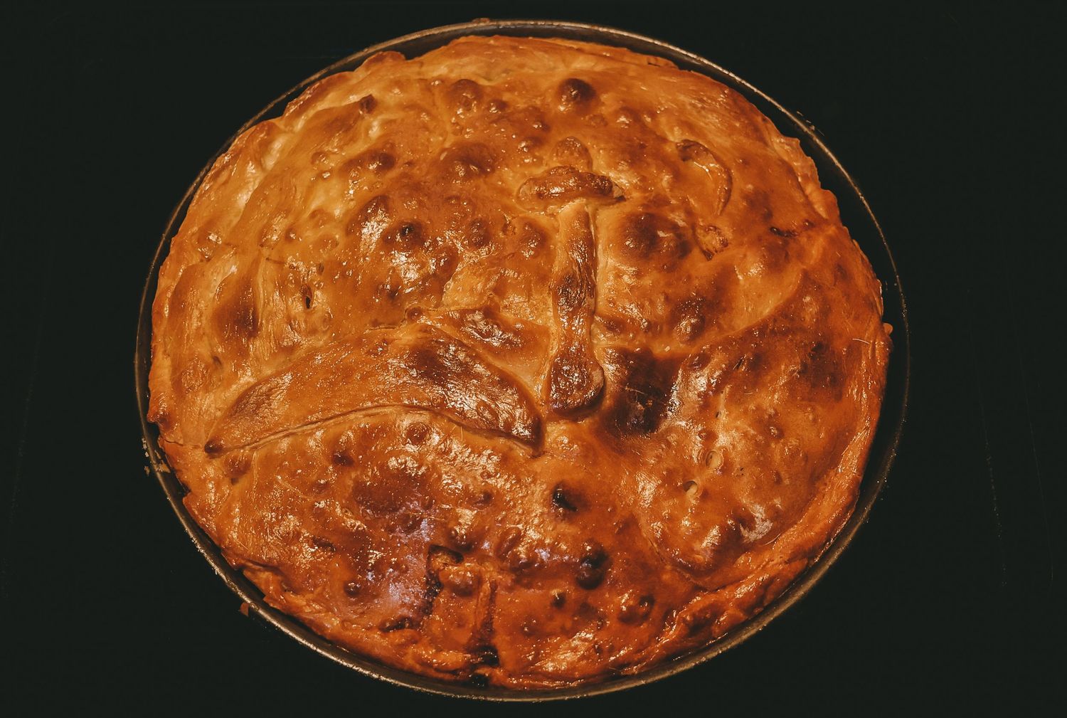 A golden brown homemade pie with a flaky lattice top crust baked to perfect doneness in a round pie dish.