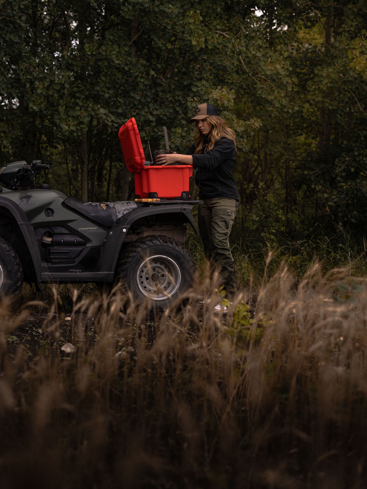 Red ATV parked among tall grass and trees during golden hour.