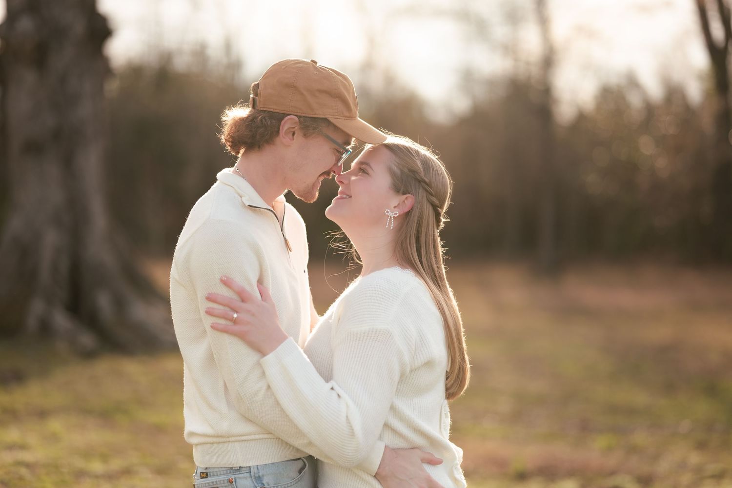 Two people in white sweaters embrace closely in soft golden sunlight with blurred nature background.