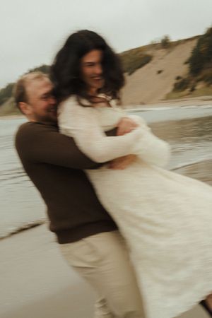 A couple in wedding attire dances and spins on a beach at sunset in a romantic blur of motion.