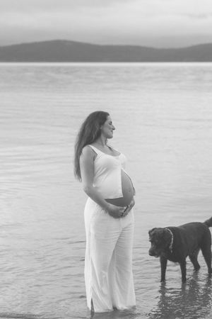 Black and white beach maternity photos showing a couple and their dog enjoying a serene moment by the water.