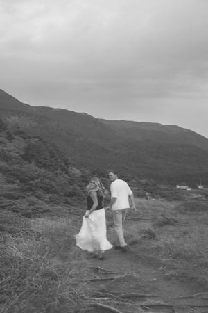 A black and white sequence of two people walking together on a hillside path with mountains in the background.
