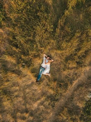 Aerial drone view of someone lying in golden grass field surrounded by dry vegetation during sunset.