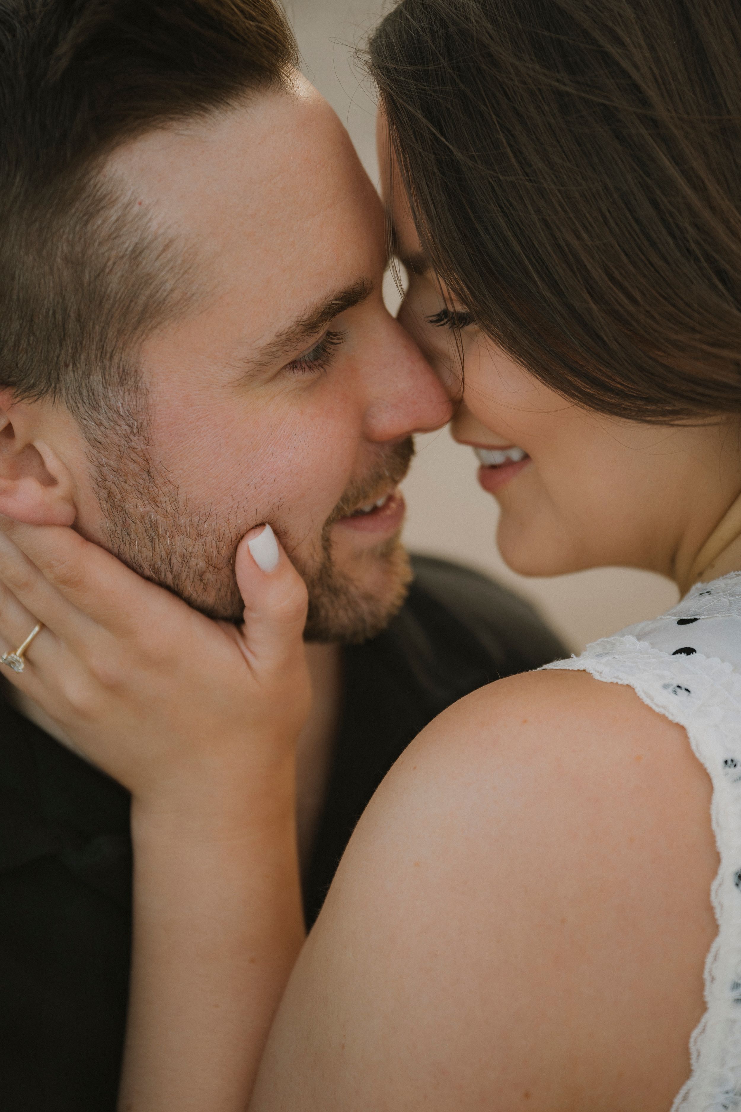 A couple shares an intimate moment, foreheads touching and smiling, as the woman gently cups the man's bearded face.