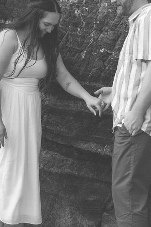 Children in white dresses and casual wear gather near a dark stone wall in a black and white photograph.
