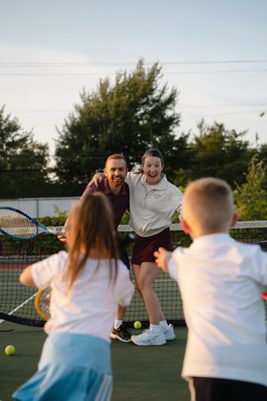 A group of friends playing tennis together on an outdoor court at sunset.
