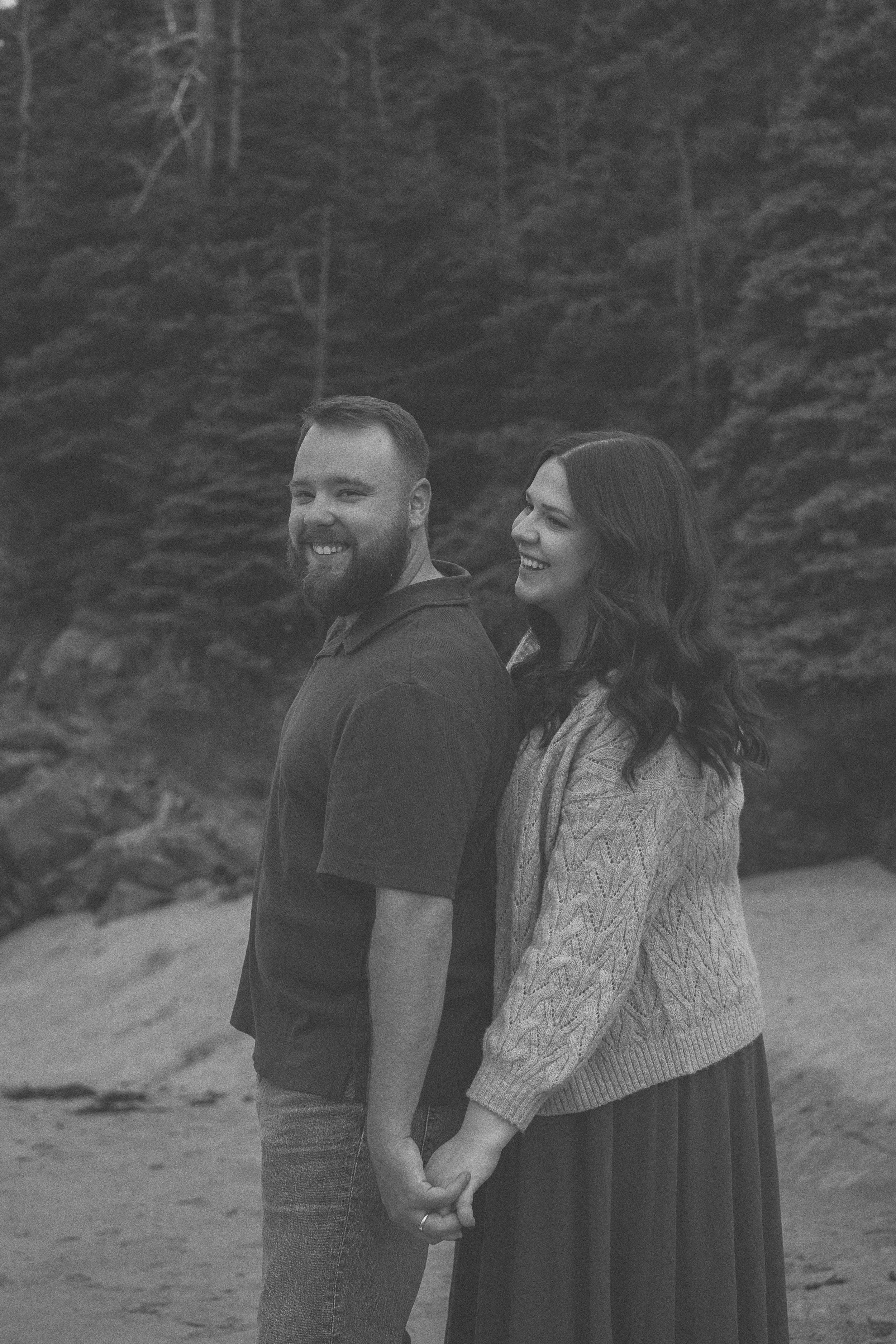 A couple shares a joyful moment together on a misty beach in black and white photography.