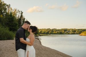 A couple shares a romantic moment at sunset on a sandy beach beside a tranquil lake.