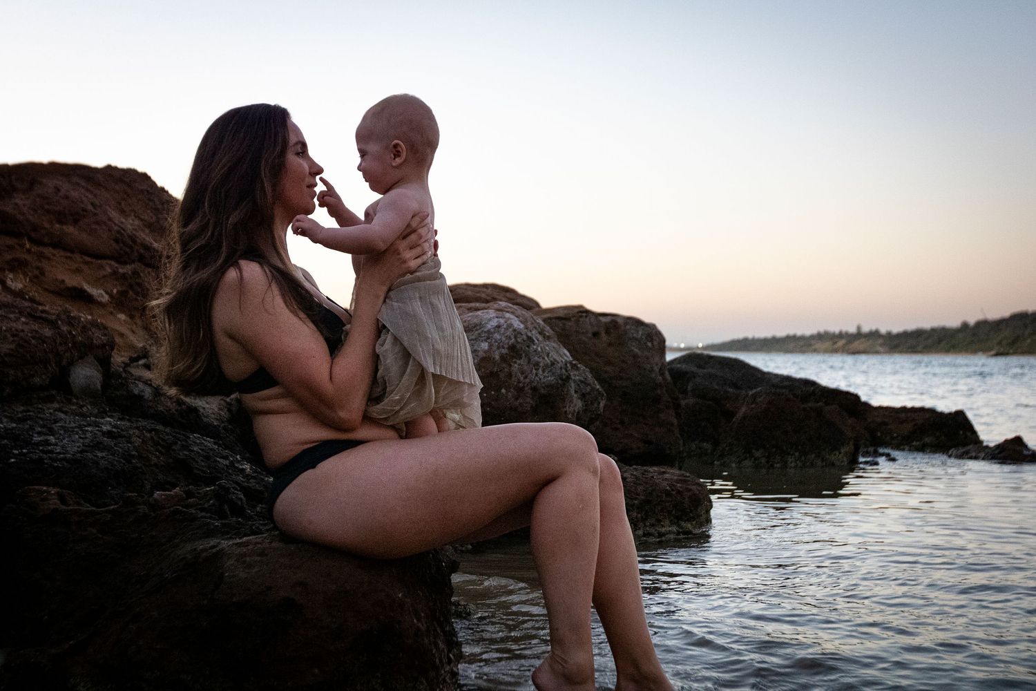 A tender moment between parent and child on coastal rocks at sunset.