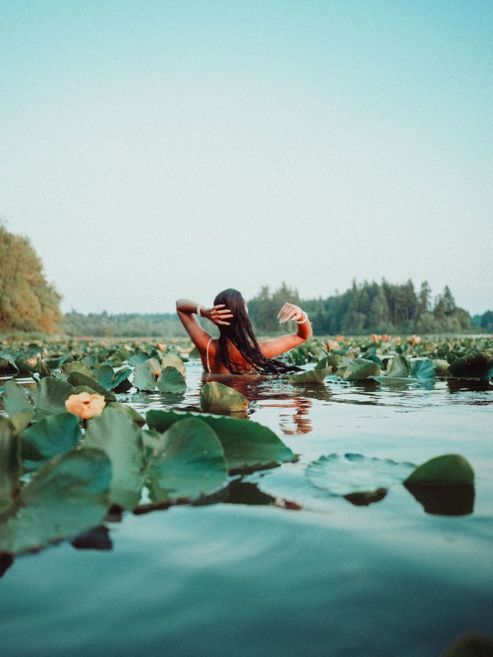 A person floating peacefully in cool water among lily pads on a serene summer day at a lake.