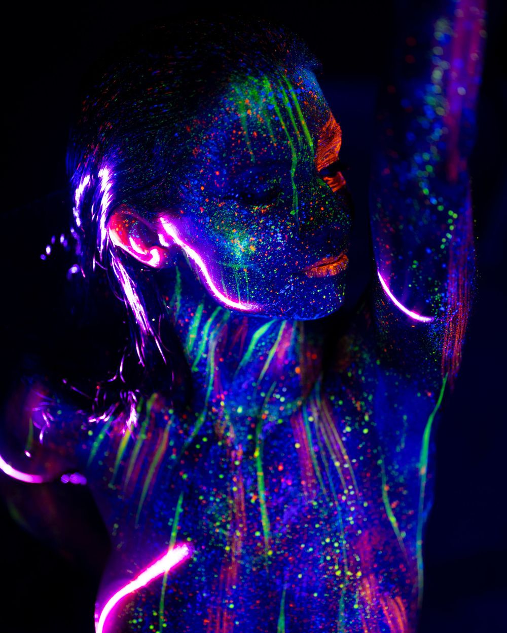 Artistic portrait illuminated with neon ultraviolet paint creating a mystical effect with blue and purple glowing patterns on a model.