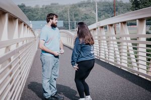Two people hold hands while walking along a wooden boardwalk on a cloudy day.