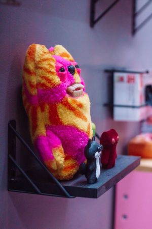 A sequence of photos showing a colorful fuzzy plush toy with pink and orange stripes sitting on a dark surface.