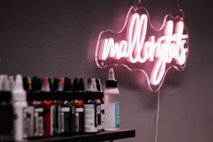 Pink neon sign illuminates bottles on dark shelves in a dimly lit bar setting.