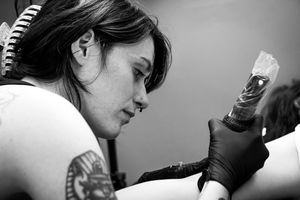 Black and white image of a tattoo artist wearing gloves while working in their studio.