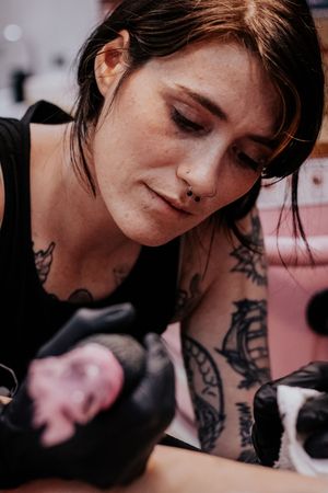 A series of close-up images showing someone getting a tattoo in dark clothing against a pink background.