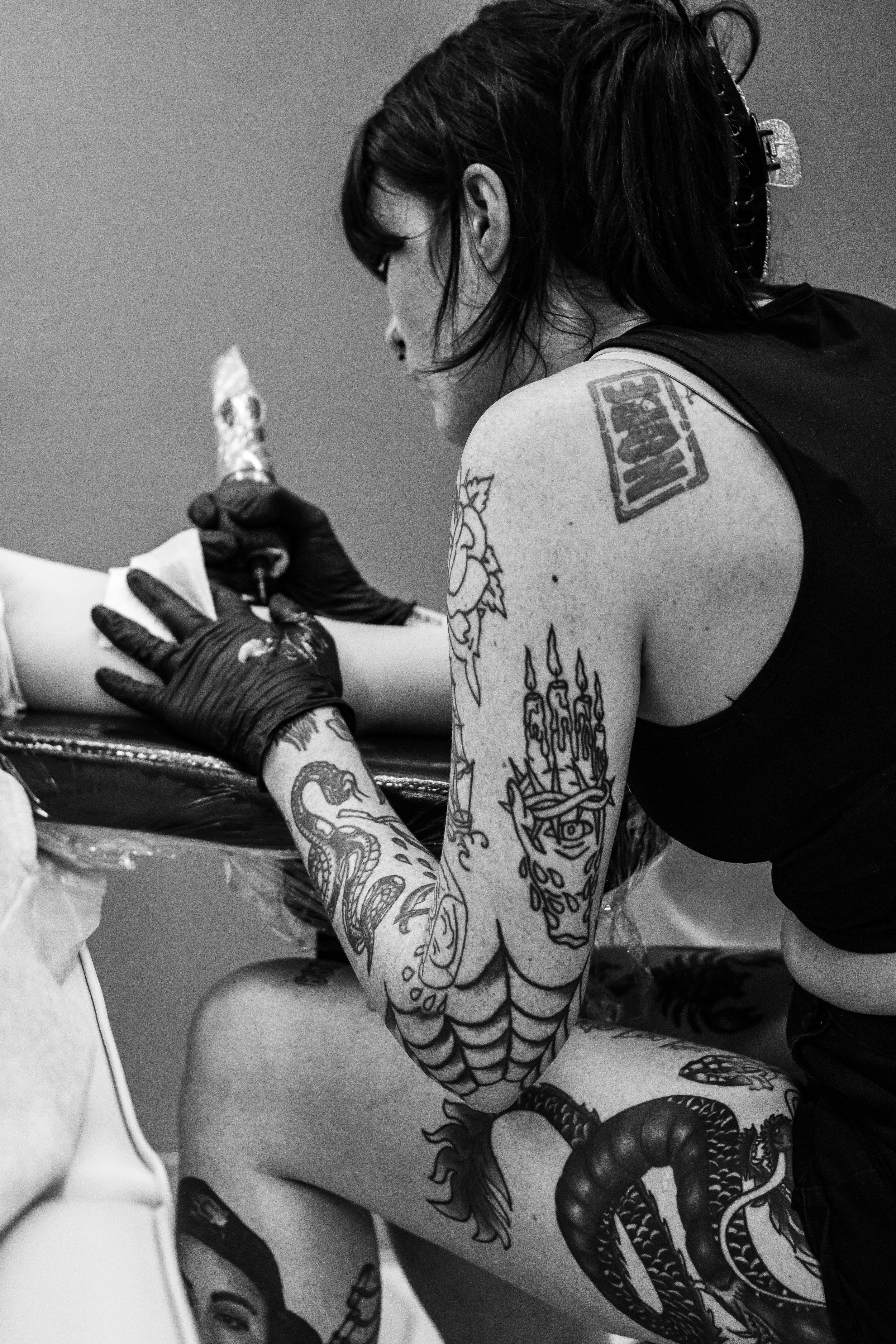Artist uses a brush to paint intricate traditional henna designs in black ink on someone's back.