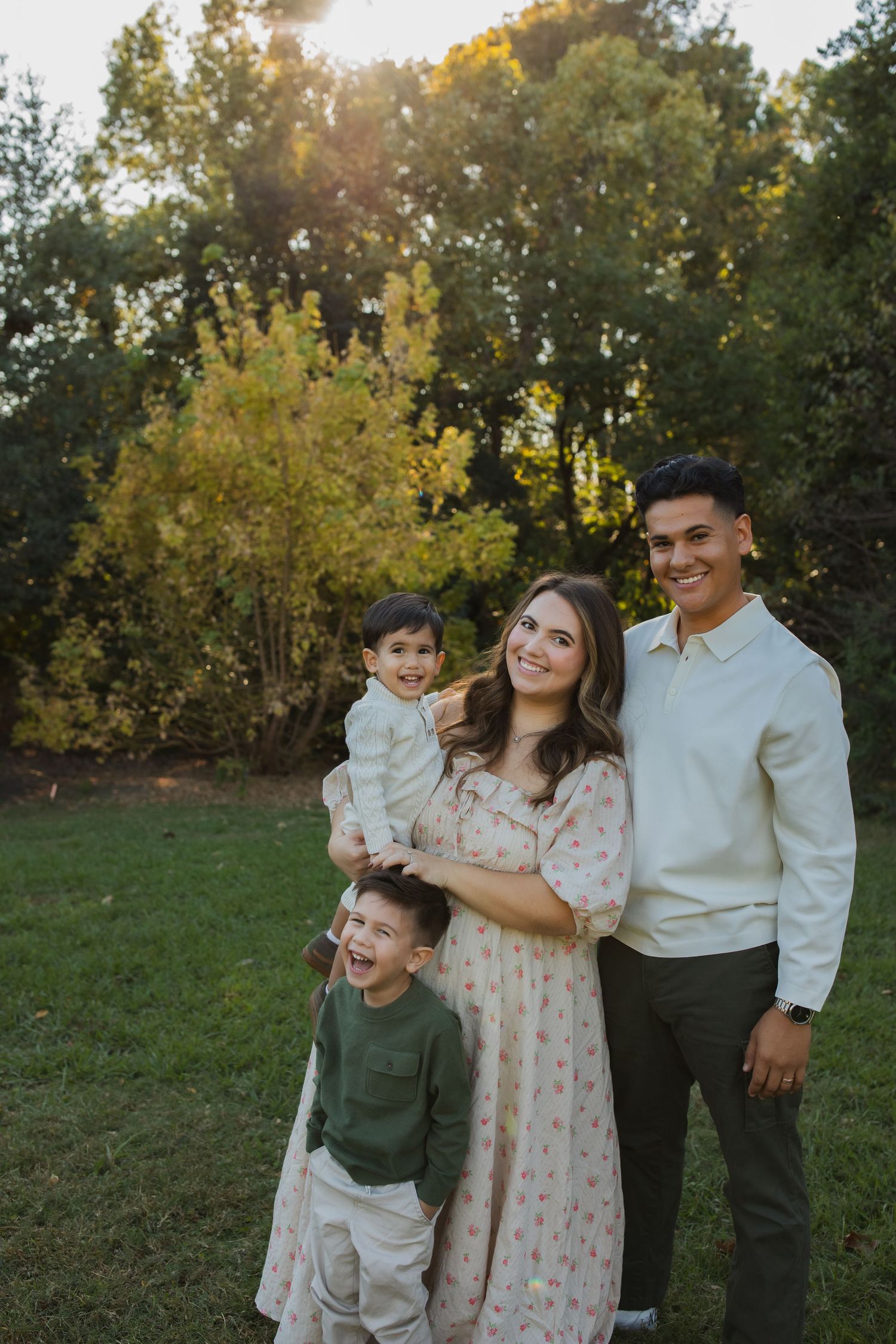 A family of four poses together outdoors during golden hour with fall foliage in the background.