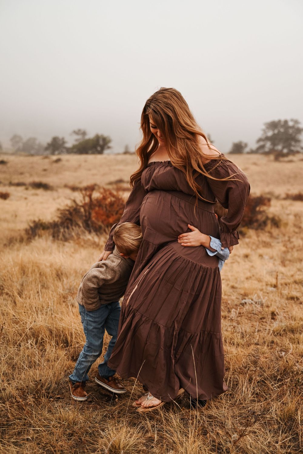 Brown dress flowing in wind during rustic family photo session in autumn field.