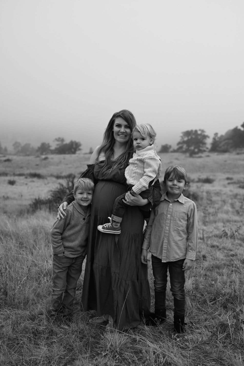 A family portrait taken in a misty field with three children and parent wearing a long dress.