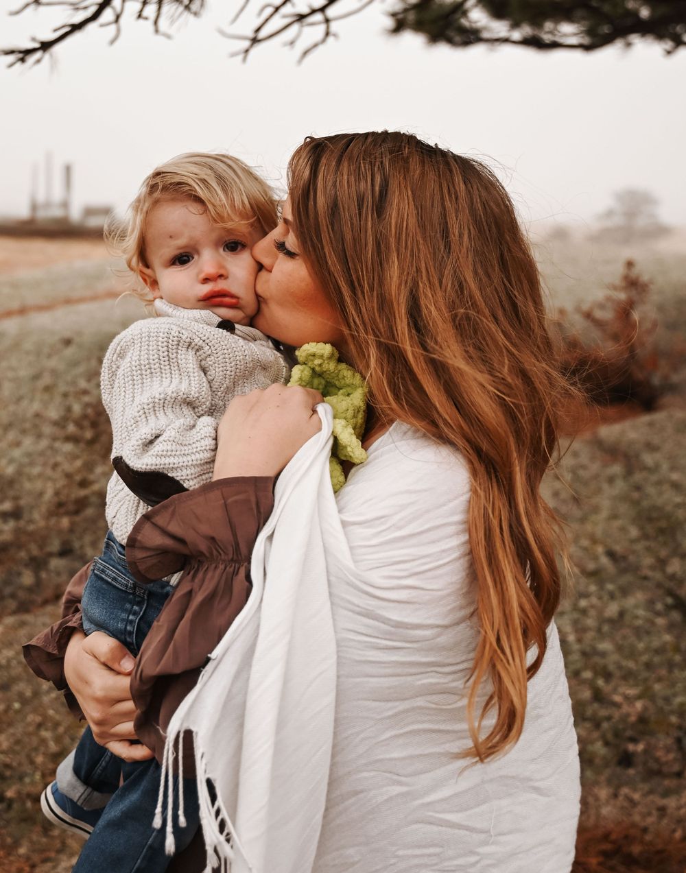 Tender moment between parent and child in white and brown outfits outdoors.