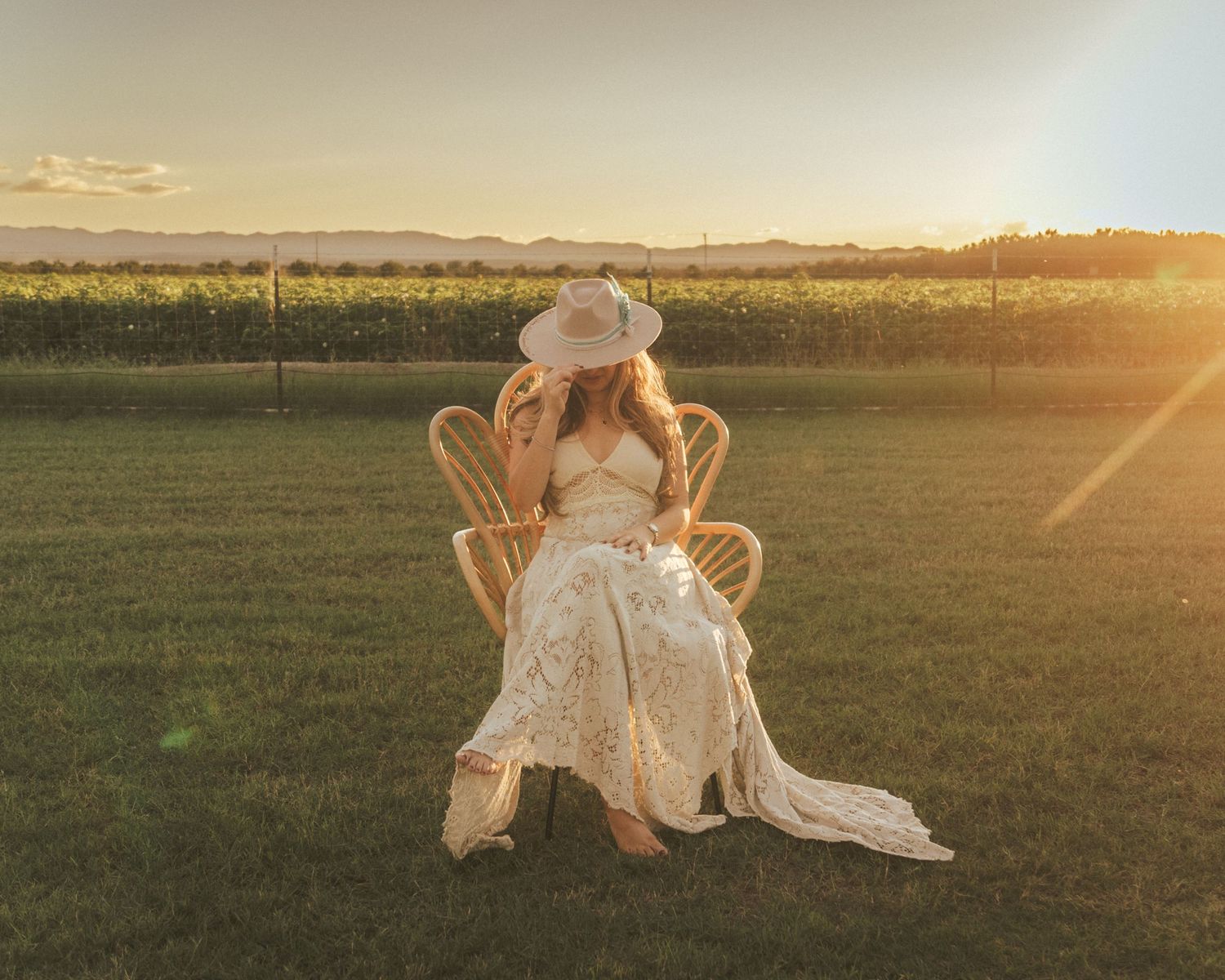 A romantic couple sits outdoors on a blanket during golden hour, sharing a tender moment with white flowers between them.