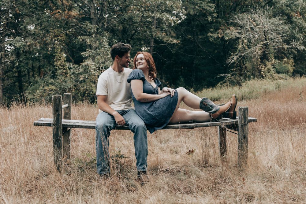 A couple sits together on a rustic wooden bench in a scenic autumn meadow.