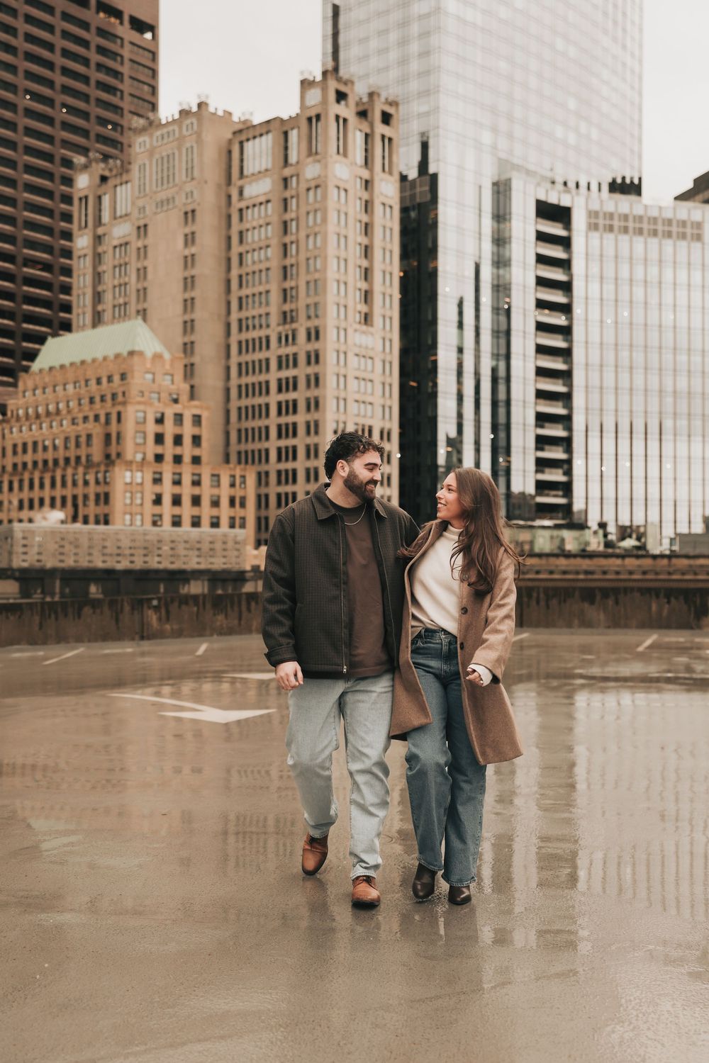 A couple walking and dancing together in front of modern glass buildings on a rainy city street.