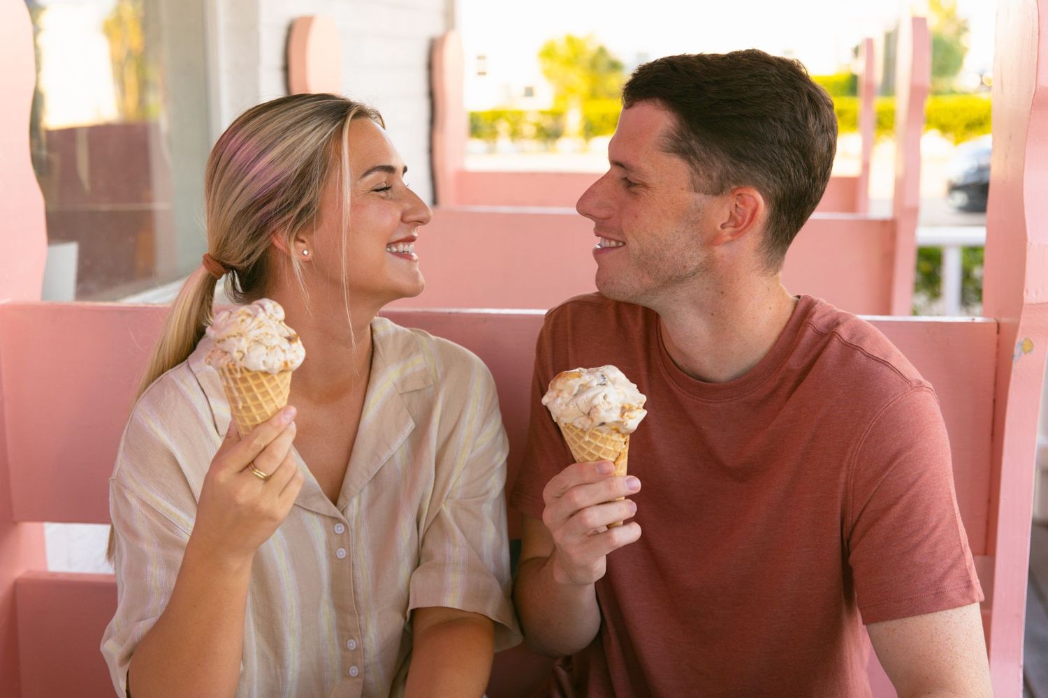 Happy couple laughing while holding ice cream cones at an outdoor cafe.