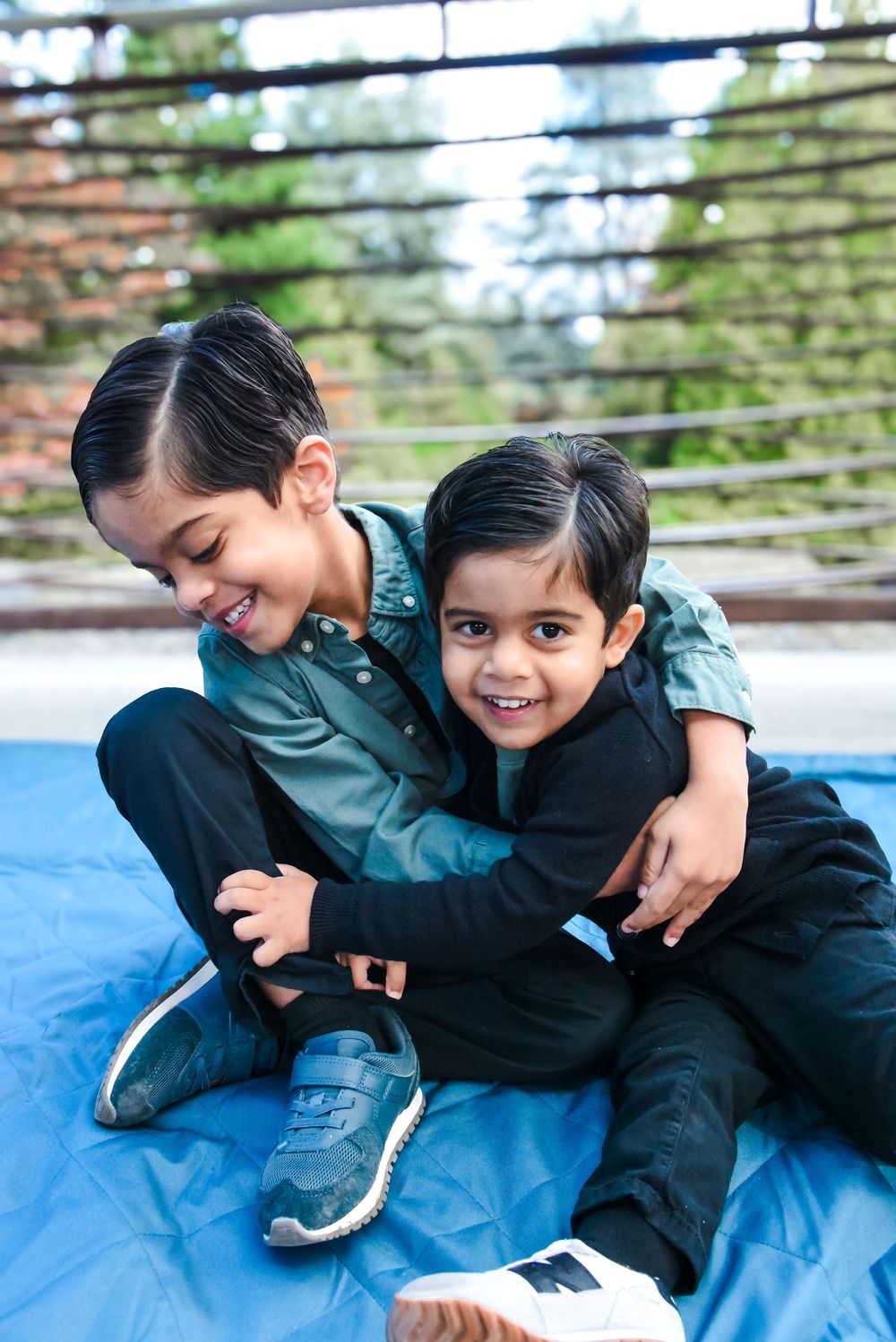 Two children in dark jackets playfully wrestling and laughing together on a blue mat.