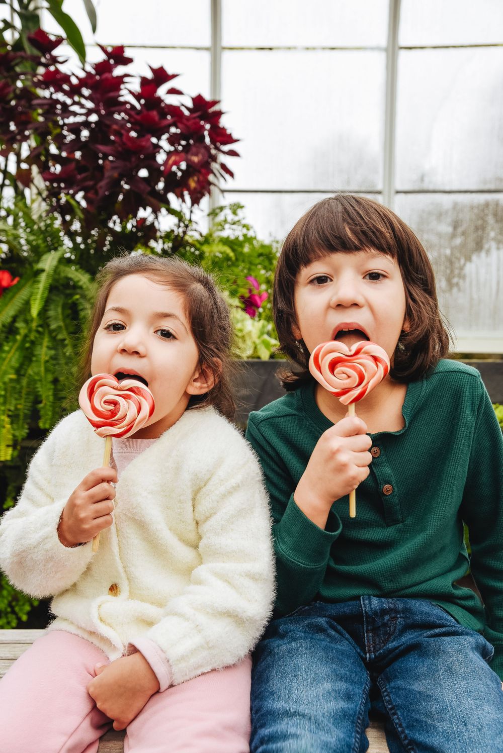 Two children enjoy heart-shaped lollipops while sitting together.
