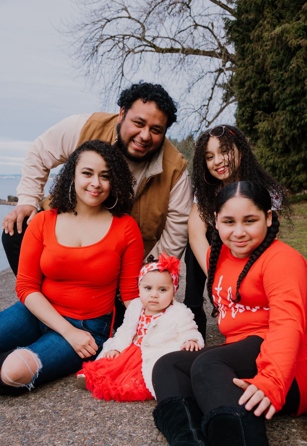A family in matching red and neutral outfits poses together on a rocky beach during a photo session.