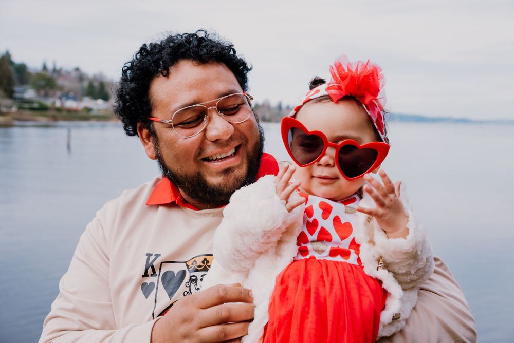 A couple poses playfully with a bright red Elmo puppet against a coastal backdrop.