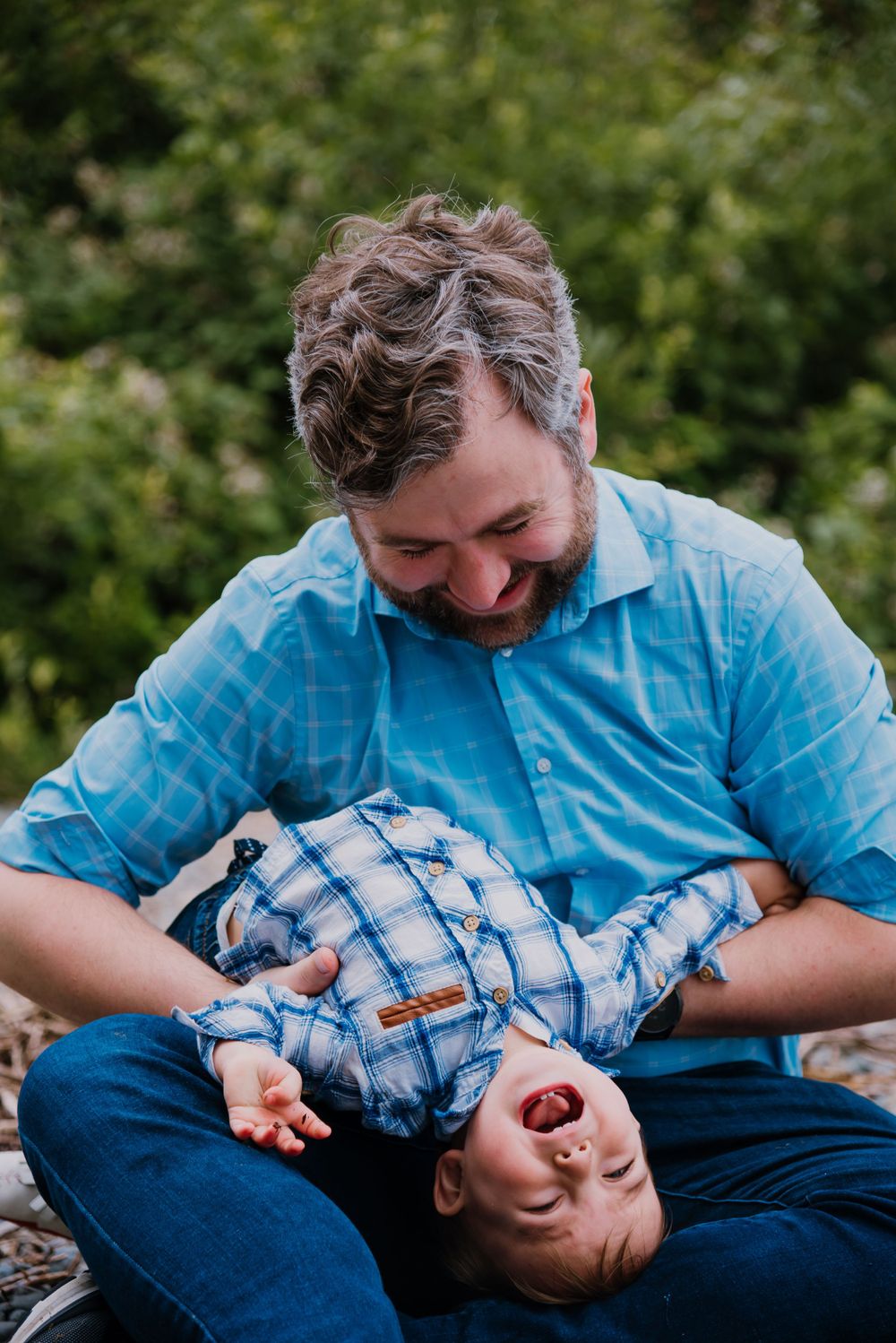A playful moment between parent and child wearing matching blue plaid shirts outdoors.