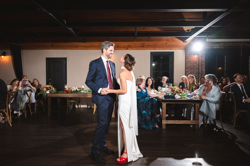 Newlyweds share their first dance in a dimly lit reception venue surrounded by wedding guests at Drowned Lands Brewery Warwick, NY.