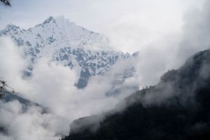 Misty mountain peaks covered in snow with low-hanging clouds creating a moody atmosphere.