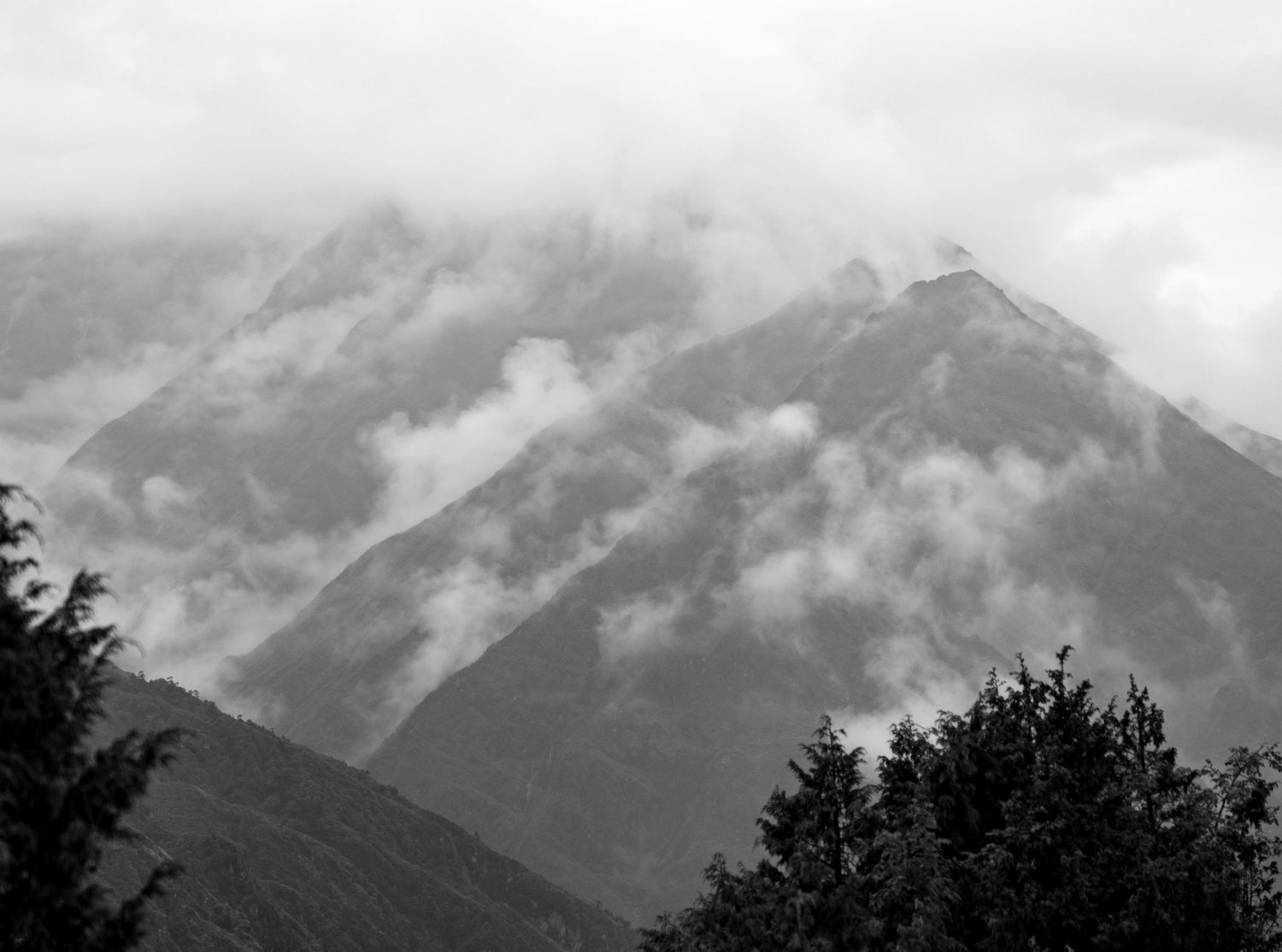 Silhouetted mountain range shrouded in clouds with dramatic lighting and misty valleys.