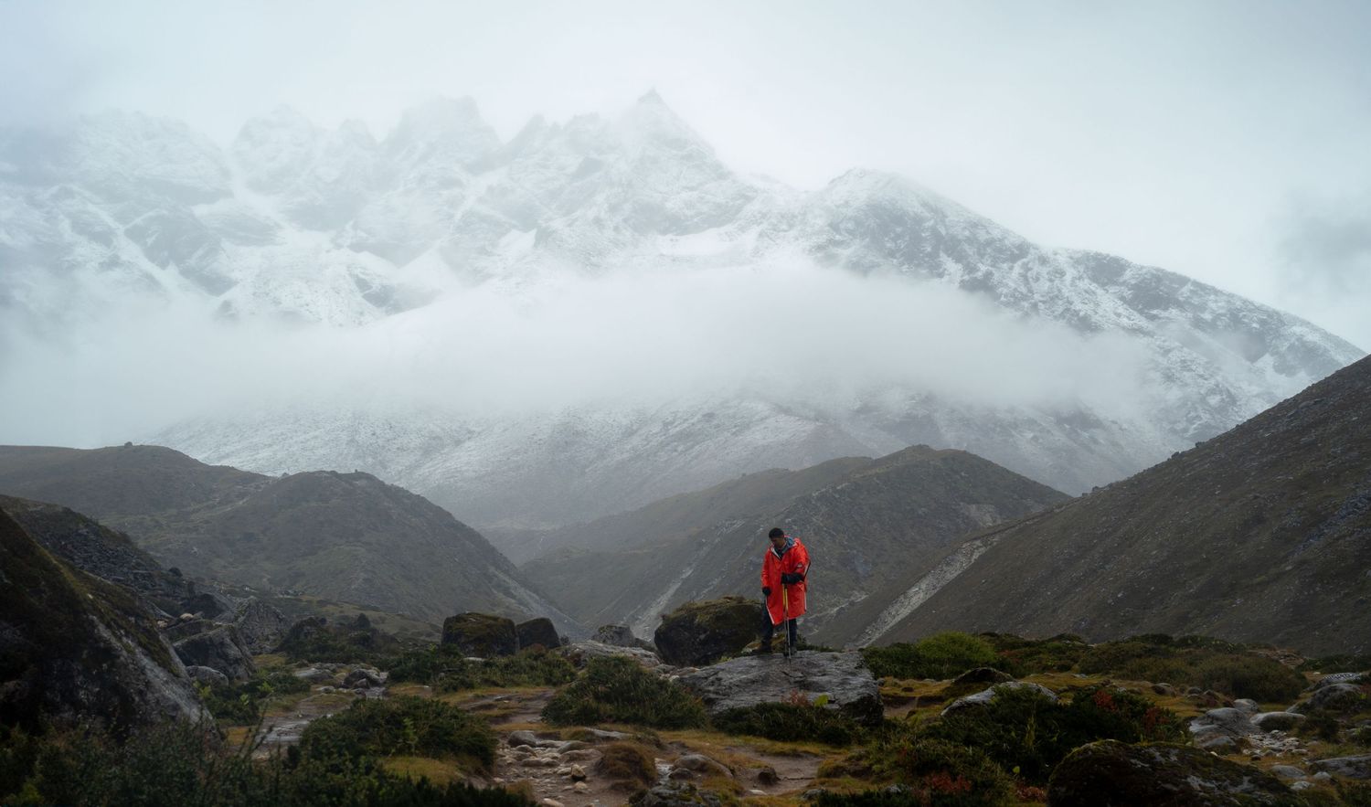 Misty mountain range with snow-dusted peaks and rocky terrain in the foreground.