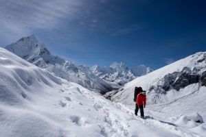 Mountaineers climbing through deep snow with jagged Himalayan peaks rising in the distance.