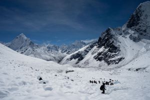 Mountaineers trek across a vast snow-covered alpine landscape surrounded by jagged peaks.