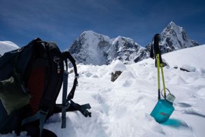 Skiers traverse a snowy mountain slope with dramatic peaks in the background under clear blue skies.
