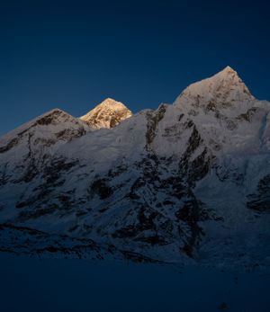 Dramatic mountain peaks catching last light at dusk with snow-covered ridges in deep blue shadows.